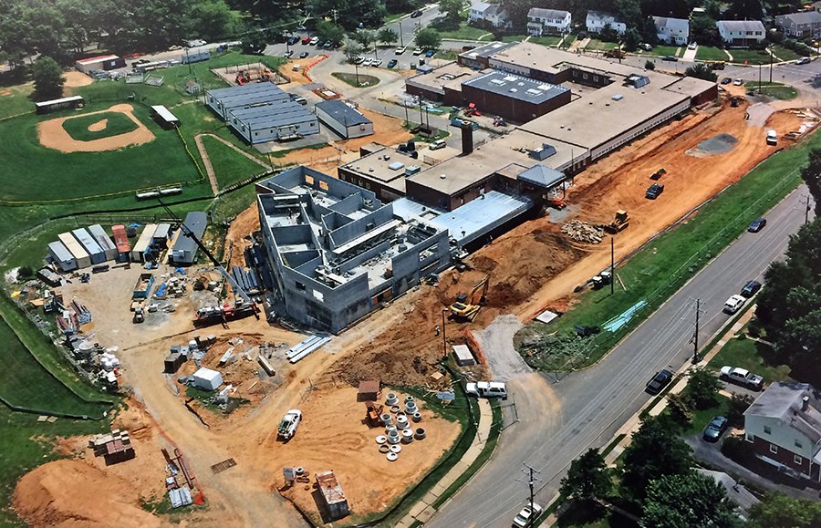 Aerial photograph of Bucknell Elementary School taken on July 20, 2016, as our school's third renovation is underway. The school is pictured from the northwest from a vantage point above University Drive. The hillside has been excavated and a new building wing is being constructed on the site. The wing is two stories tall. The cinderblock walls are in place. 