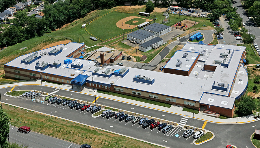 Aerial photograph of Bucknell Elementary School taken on June 20, 2017, as our school's third renovation is largely complete. The school is pictured from the northwest from a vantage point above University Drive. From the outside, the building looks finished. It has a brand new roof throughout the entire structure with blue paneling hiding the roof-top air conditioning units. The trailers are still visible behind the school. 