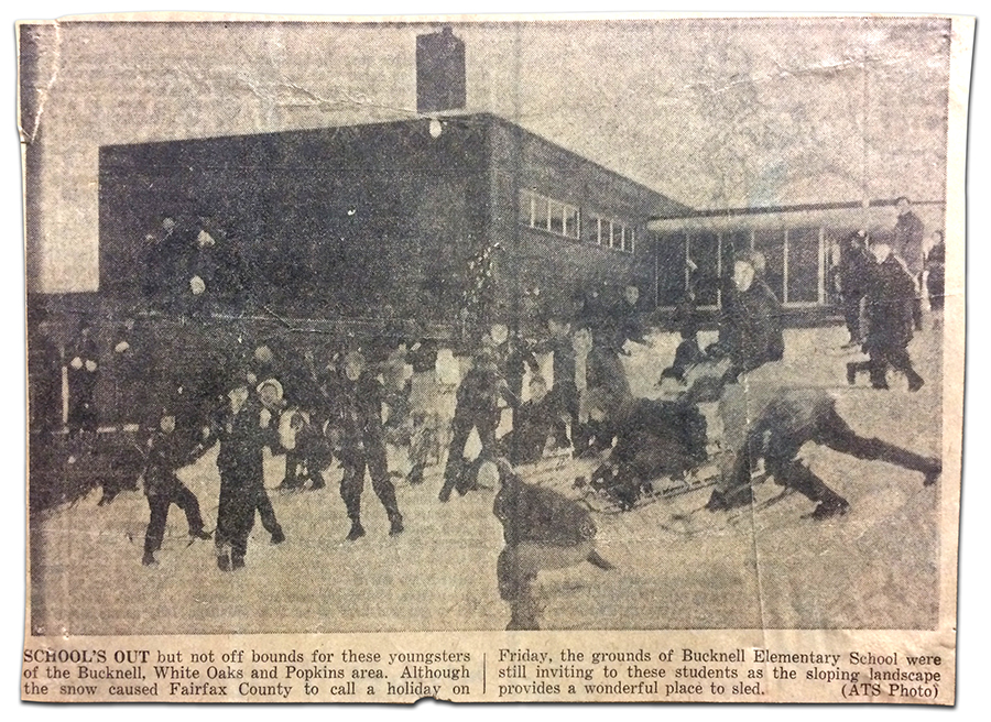 Newspaper clipping from an article about schools being closed for snow and children sledding on the hillside at Bucknell Elementary School. A black and white photograph and its caption are shown. In the photograph, a large group of children can be seen sledding on a snow-covered hill with the school in the background. The caption reads: School's Out, but not off bounds for these youngsters of the Bucknell, White Oaks, and Popkins area. Although the snow caused Fairfax County to call a holiday on Friday, the grounds of Bucknell Elementary School were still inviting to these students as the sloping landscape provides a wonderful place to sled.