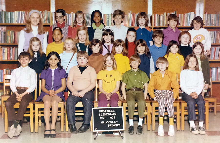 Color class photograph from 1971 to 1972 showing children from Room 14. 27 children and their teacher are pictured. The picture was taken in the library. The children are arranged in four rows, and the teacher is standing in the far back row on the left. 