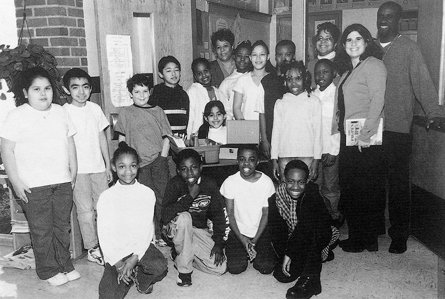 Black and white photograph from our 2000 to 2001 yearbook showing a group of students posing in front of the school store. 15 students and four adults are pictured. 